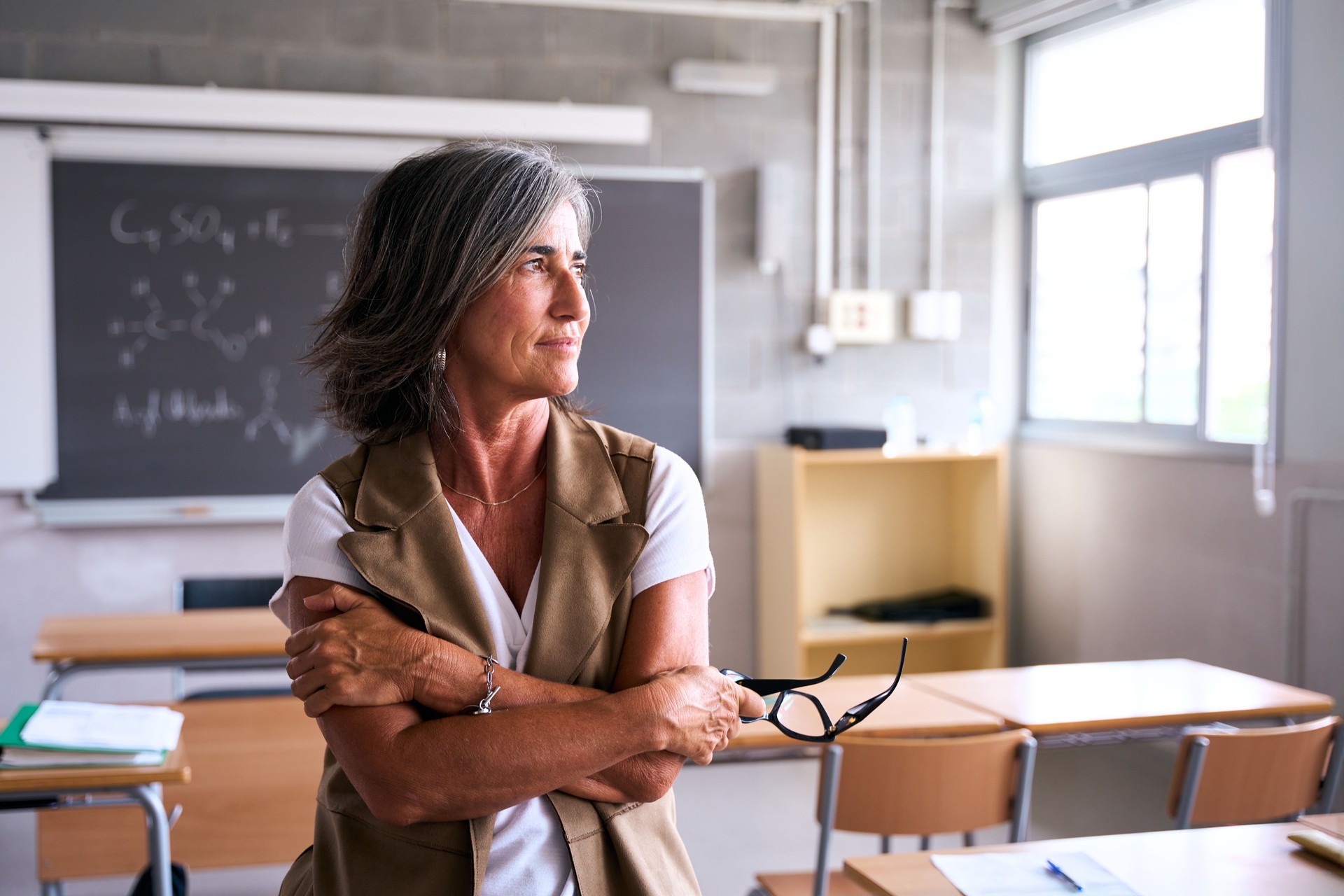 A teacher stands alone in an empty classroom, gazing thoughtfully out of the window